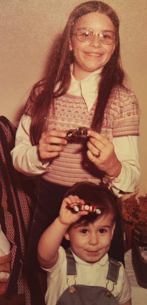 Older sister shown with younger brother in the 1970s, each holding up a Matchbox car